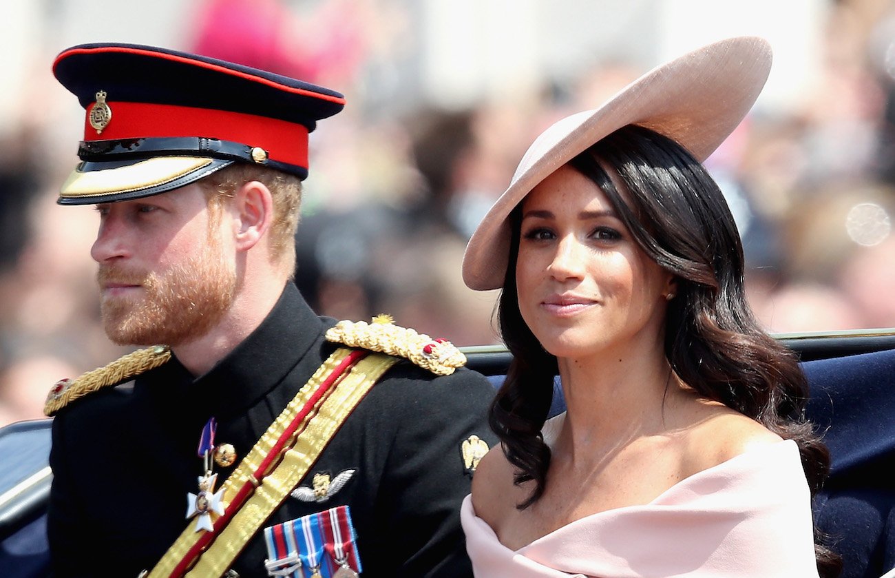 Prince Harry looks on while wearing his military uniform as Meghan Markle smiles wearing a pink hat and outfit at Trooping the Color in 2018