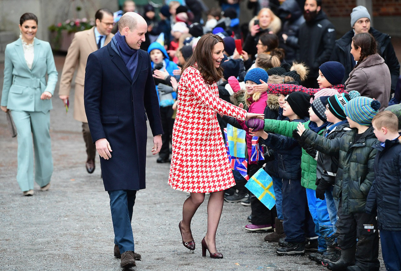 Prince William wears a blue coat as he stands next to Kate Middleton in a red and white check coat