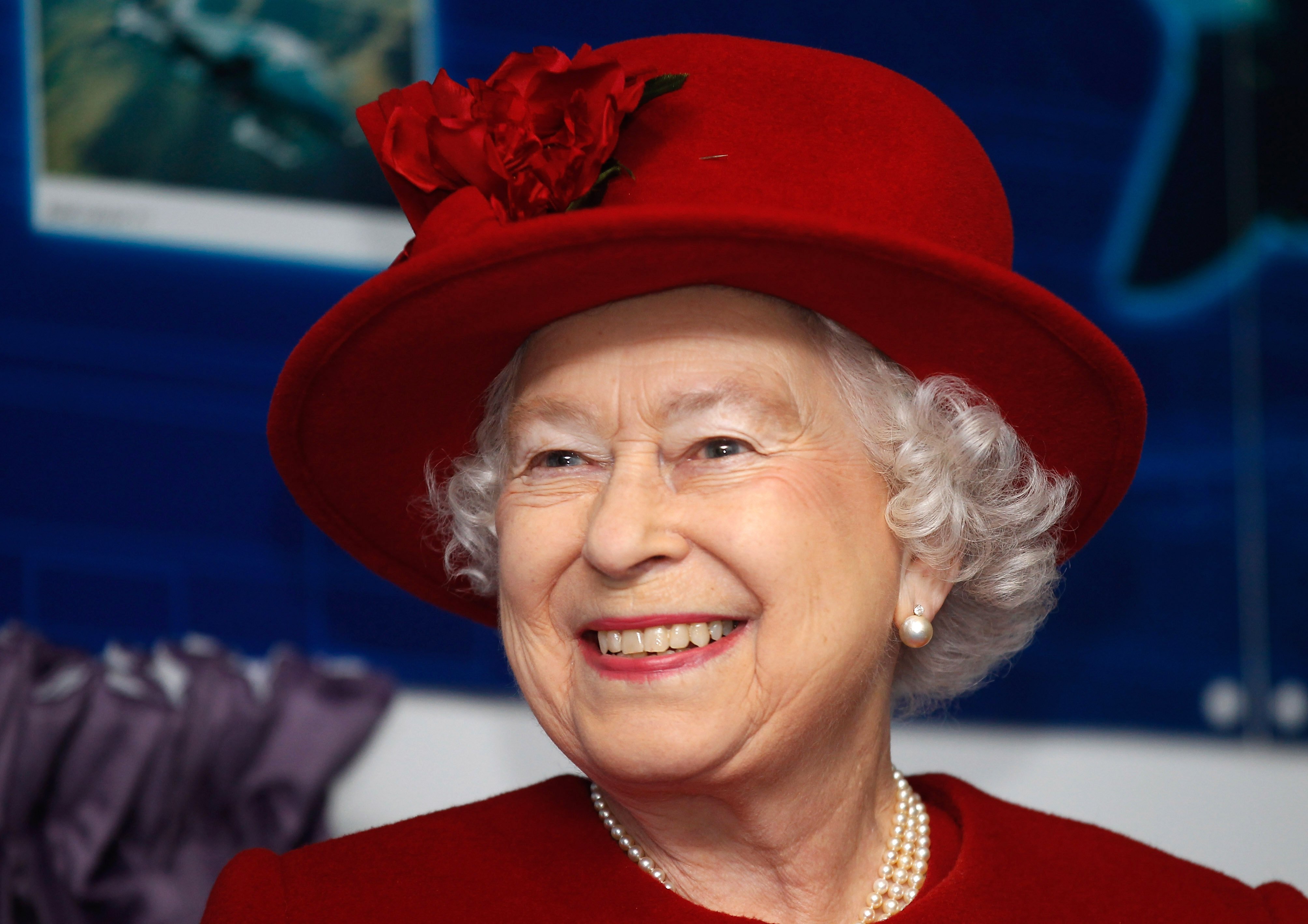 Queen Elizabeth II wearing red and smiling as she tours RAF Valley