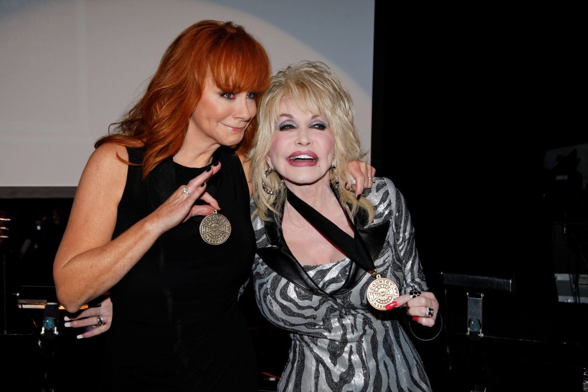 Reba McEntire poses next to Dolly Parton, both showing off medals worn around their necks