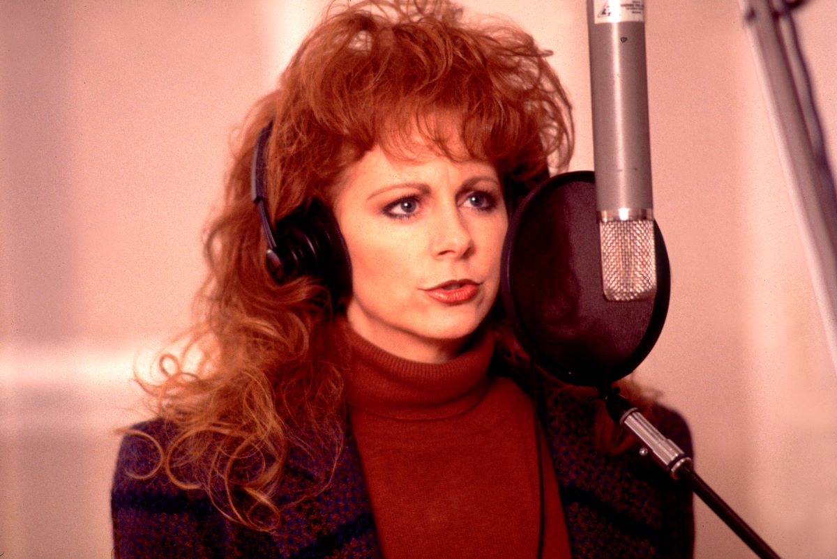 Reba McEntire wears a red turtleneck and sings into a microphone c. 1994