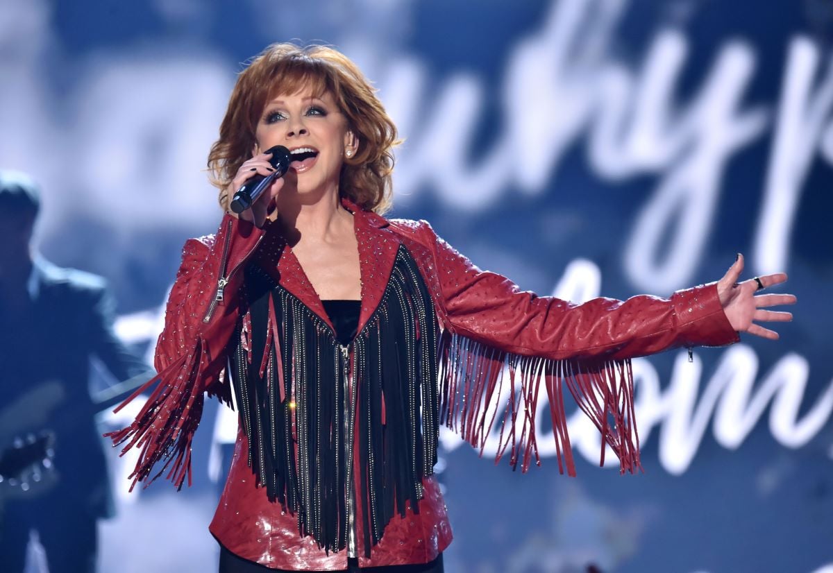 Reba McEntire in a red and black fringed jacket, holding a microphone