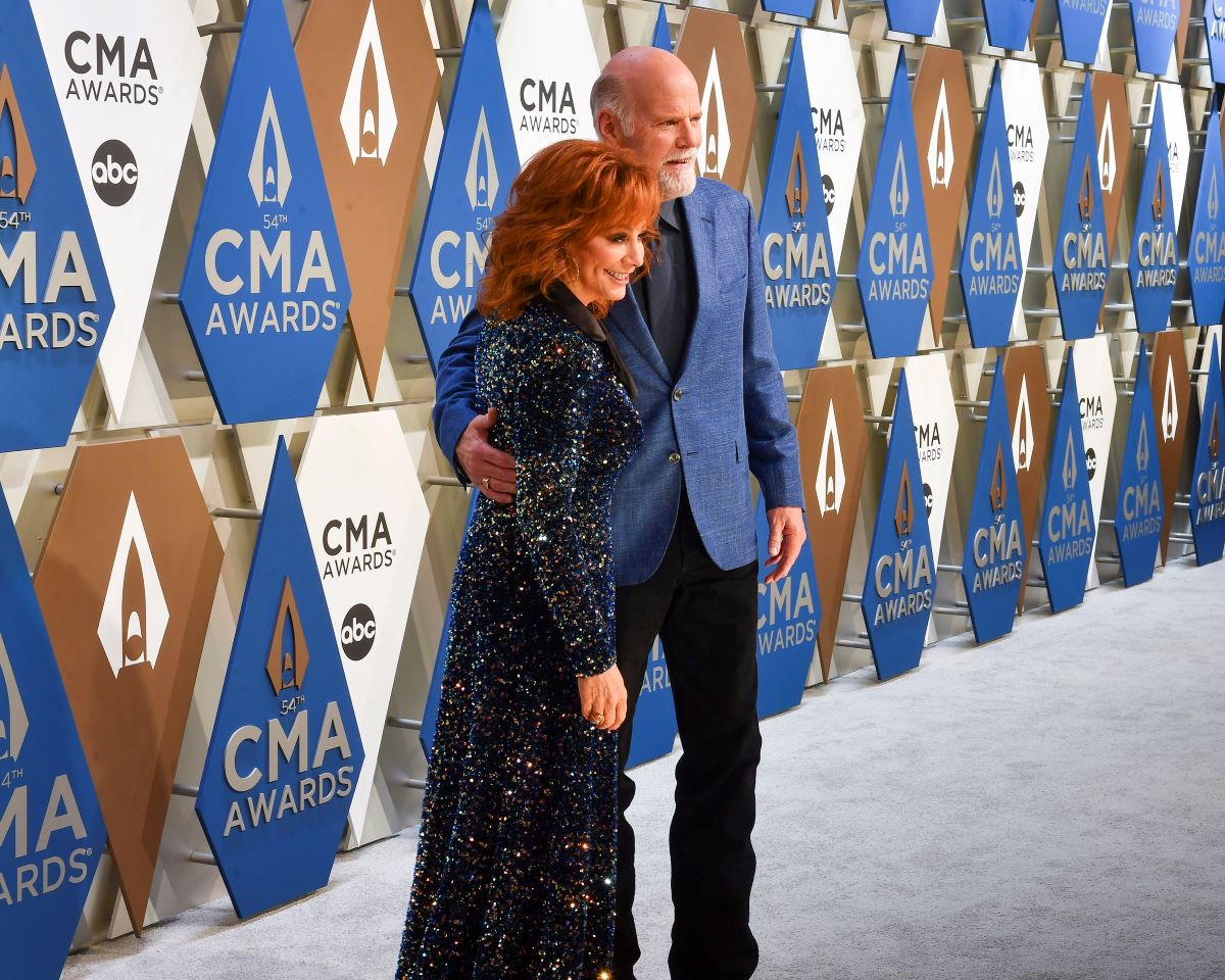 Reba McEntire in a sparkly floor length dress, standing next to boyfriend Rex Linn who is wearing a suit with a blue jacket. 