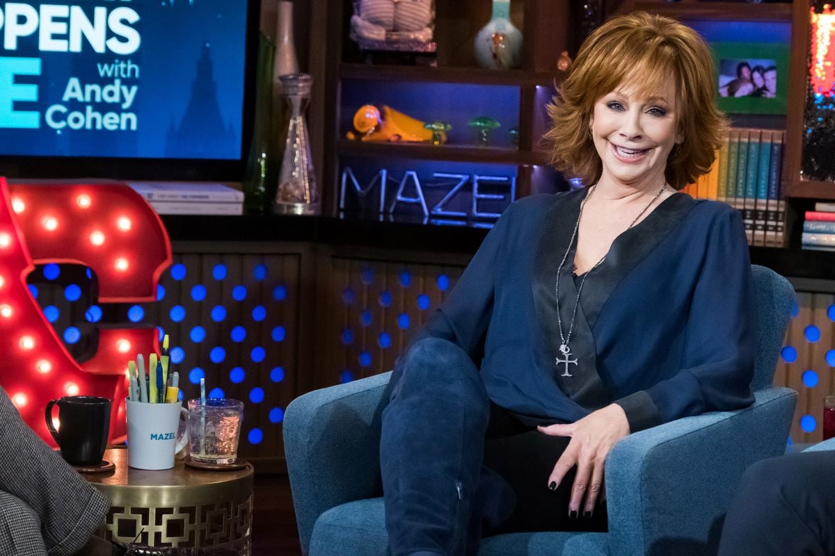 Reba McEntire seated with legs crossed, smiling