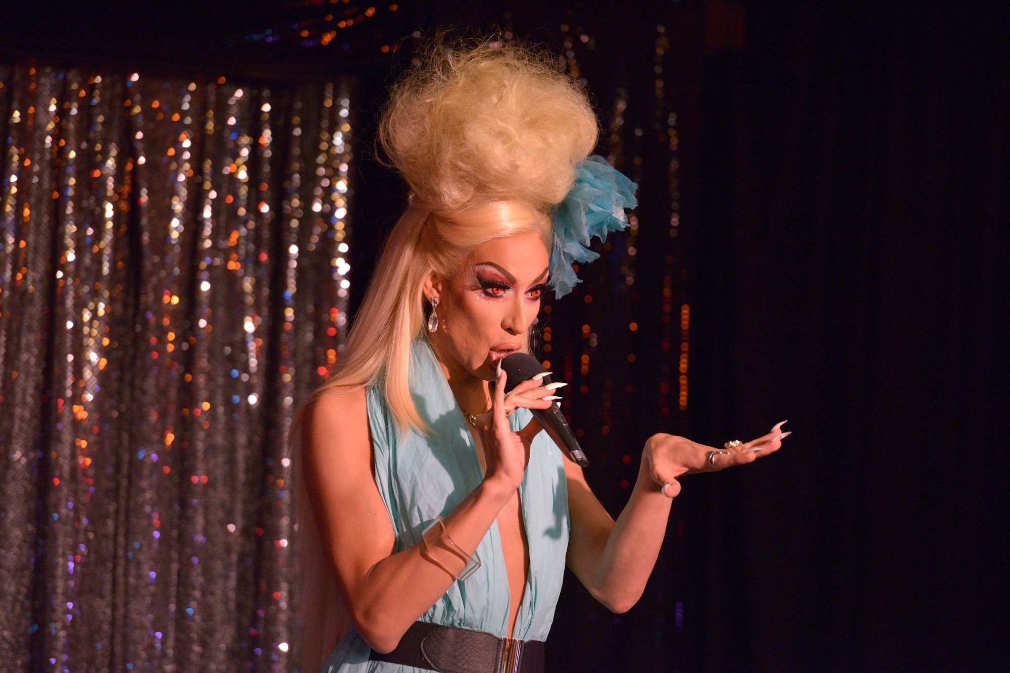 'RuPaul's Drag Race' Season 5 drag queen Alaska talking into a mic with glitter curtains in the background