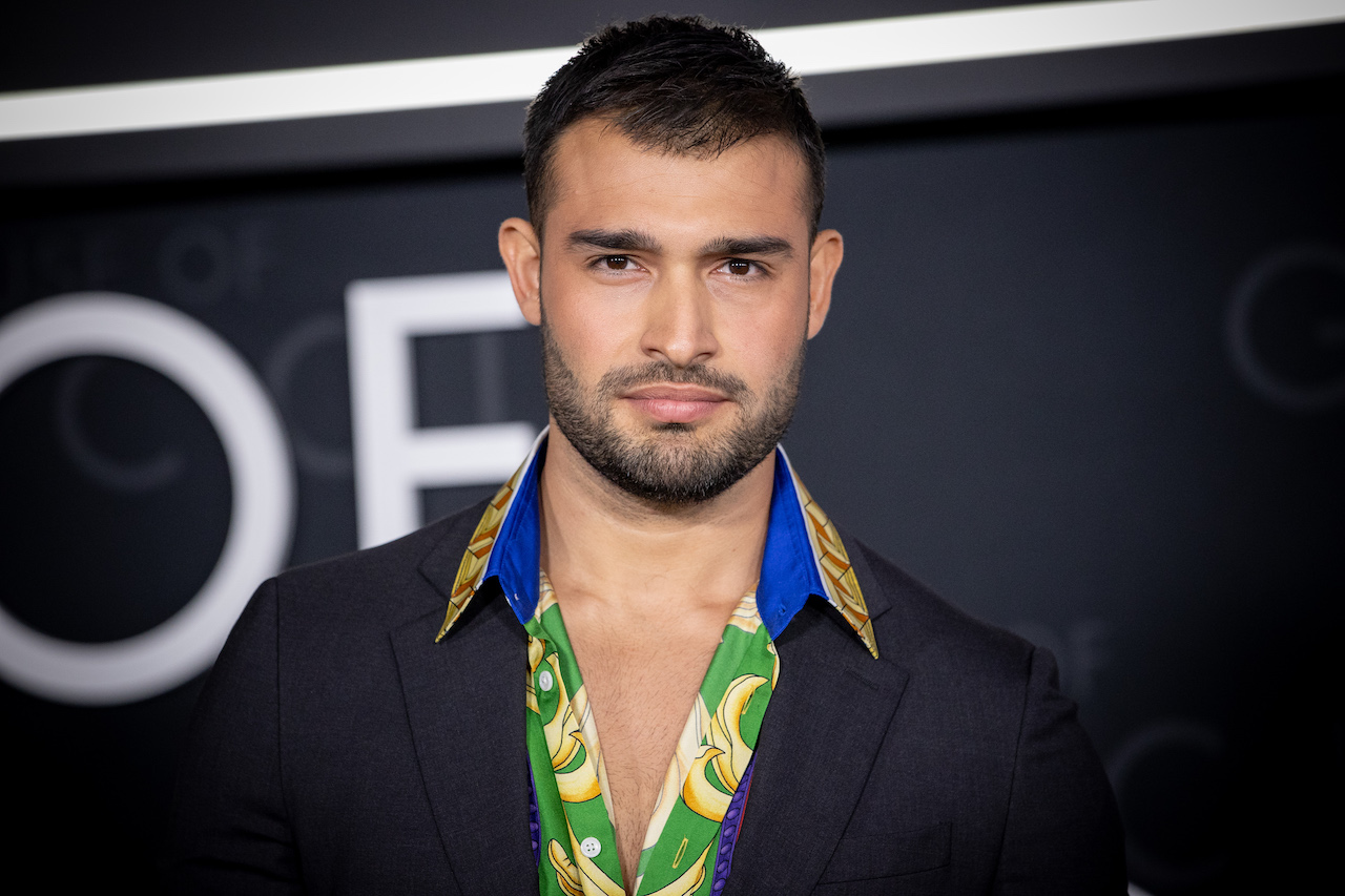 Sam Asghari poses in a colorful shirt and black jacket.