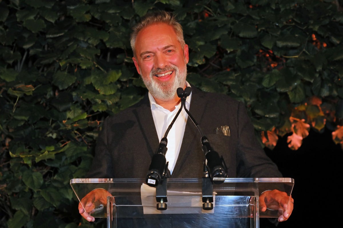 Sam Mendes smiling on stage wearing a business suit.