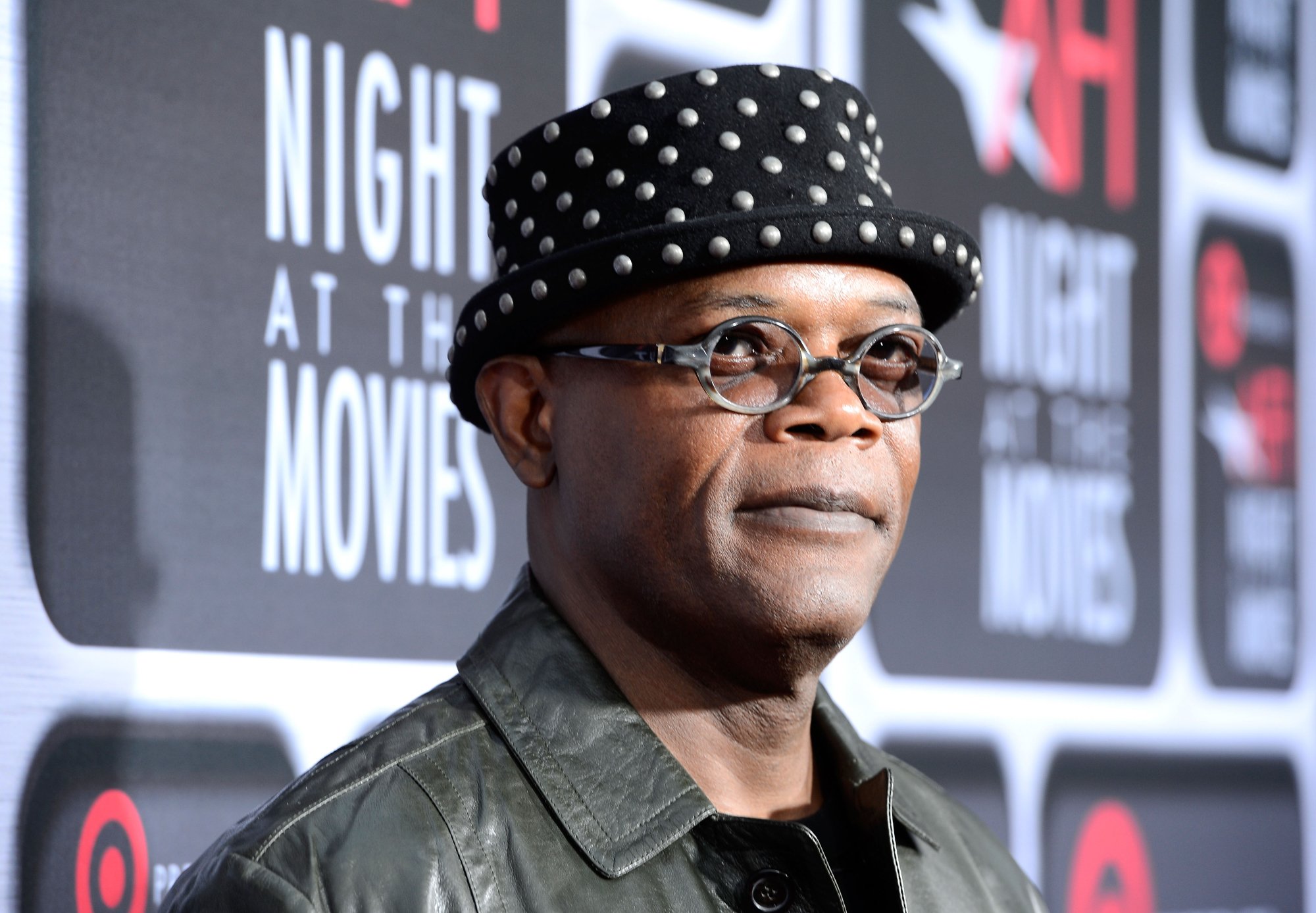 Samuel L. Jackson wearing a dotted hat and a leather jacket in front of a step and repeat