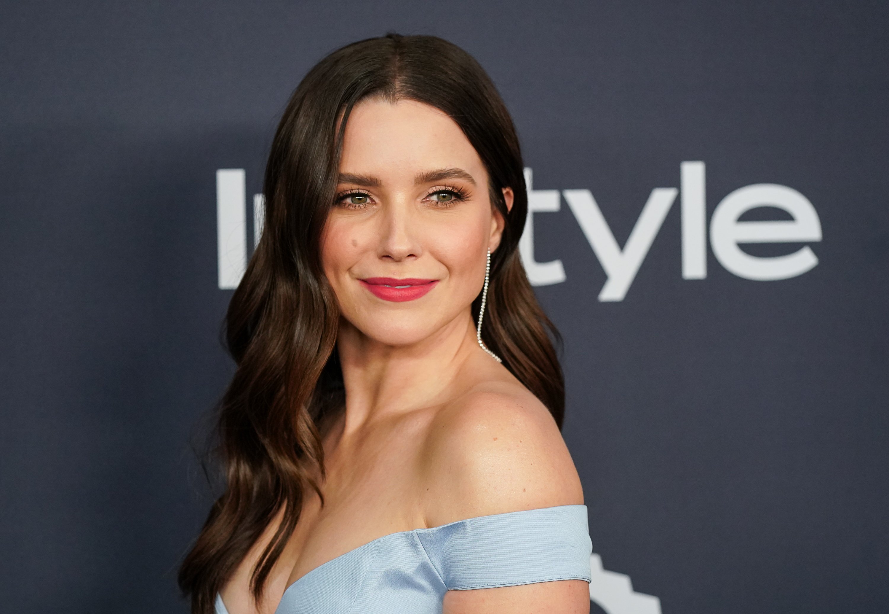 Former Chicago P.D. actor Sophia Bush smiles for a photo wearing a blue off-the-shoulder dress.