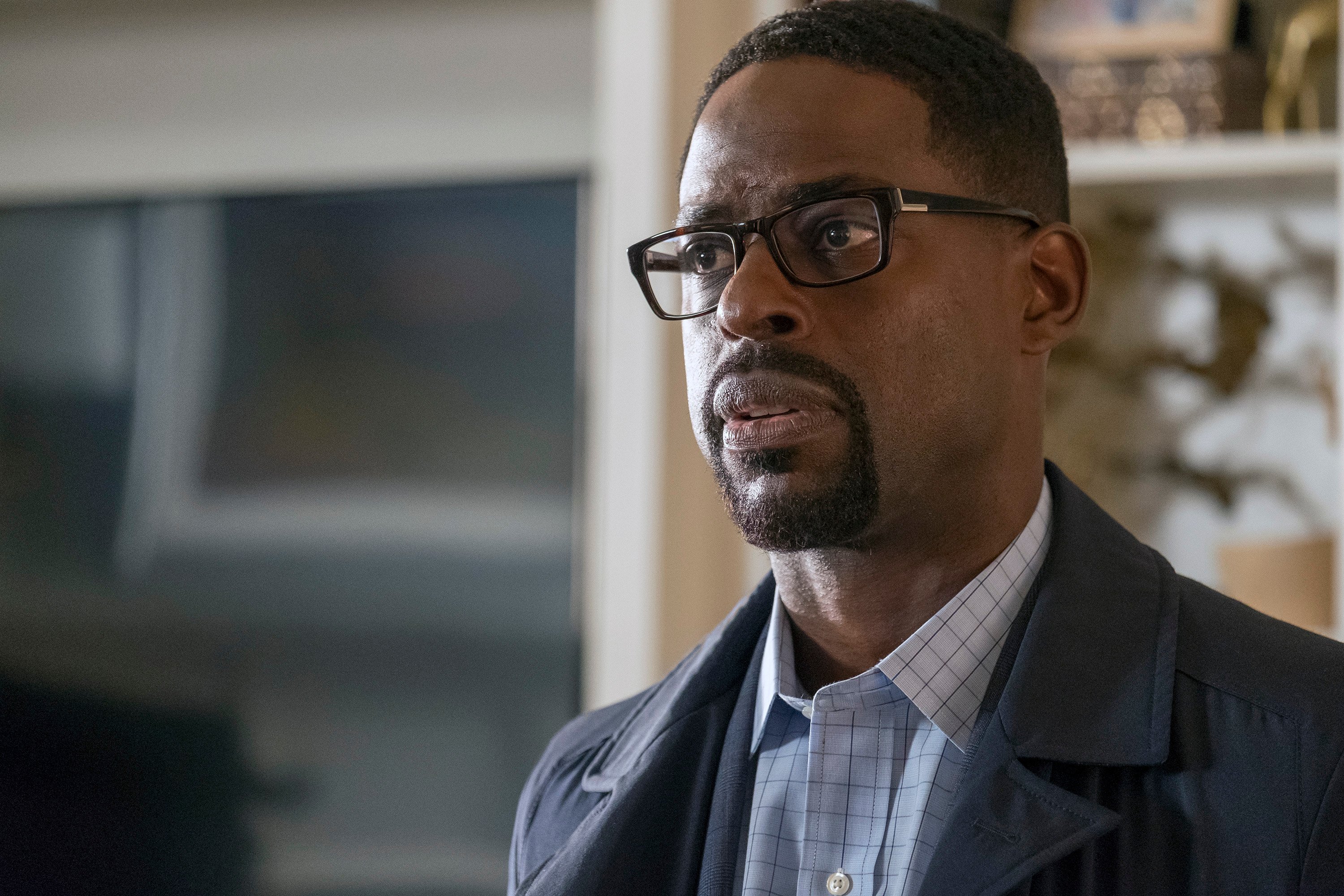 'This Is Us' Season 6 actor Sterling K. Brown, who will star in the series finale, wears a dark gray coat over a white checkered button-up shirt and a pair of black glasses as his character, Randall Pearson.