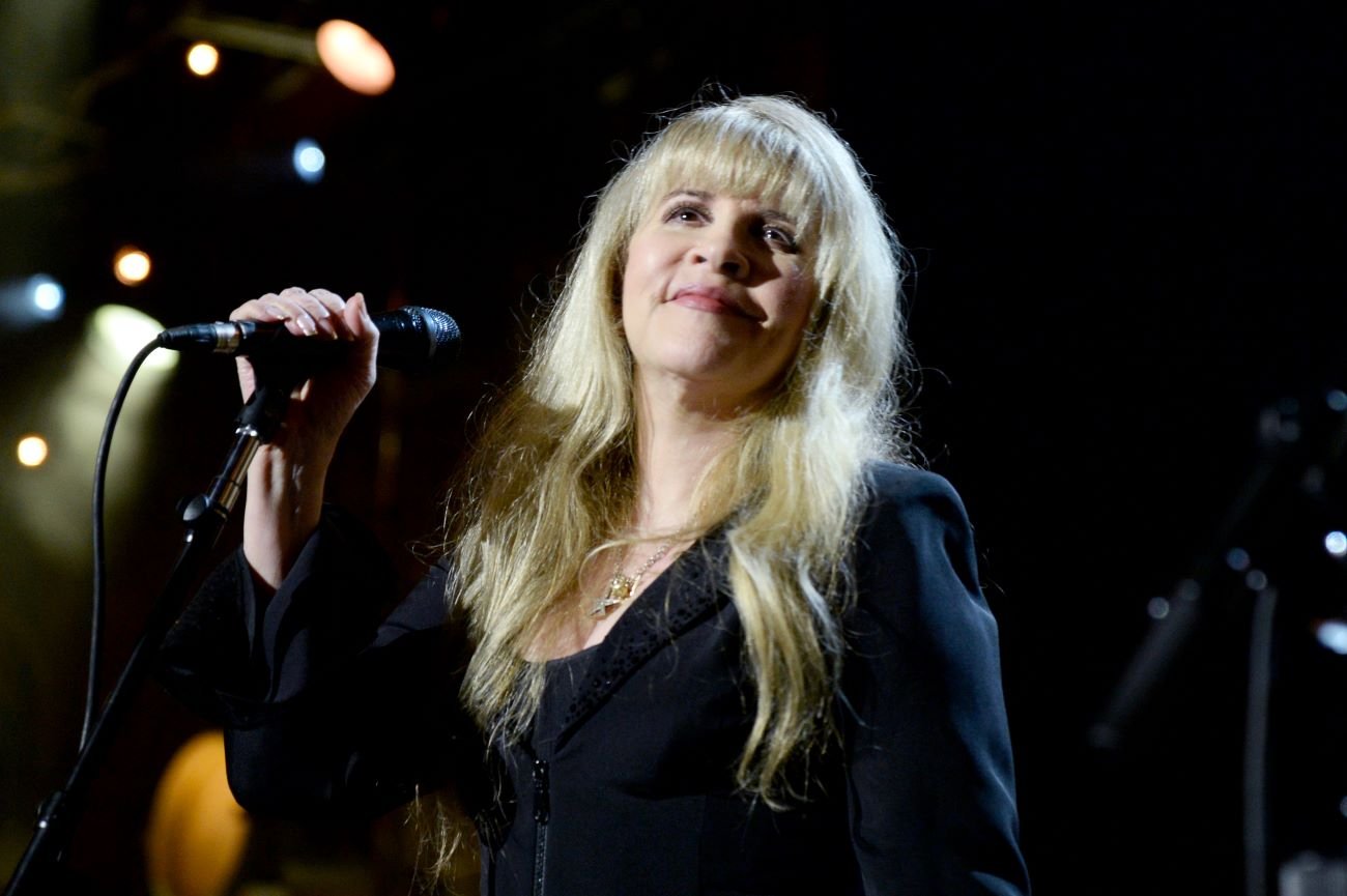 Stevie Nicks wears a black shirt and holds a microphone.