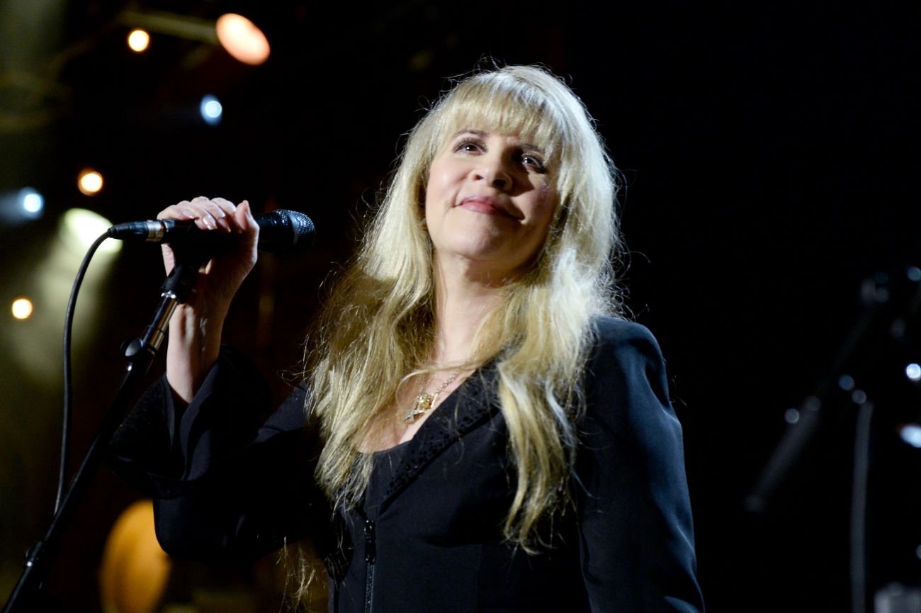 Stevie Nicks wears a black shirt and holds a microphone. 