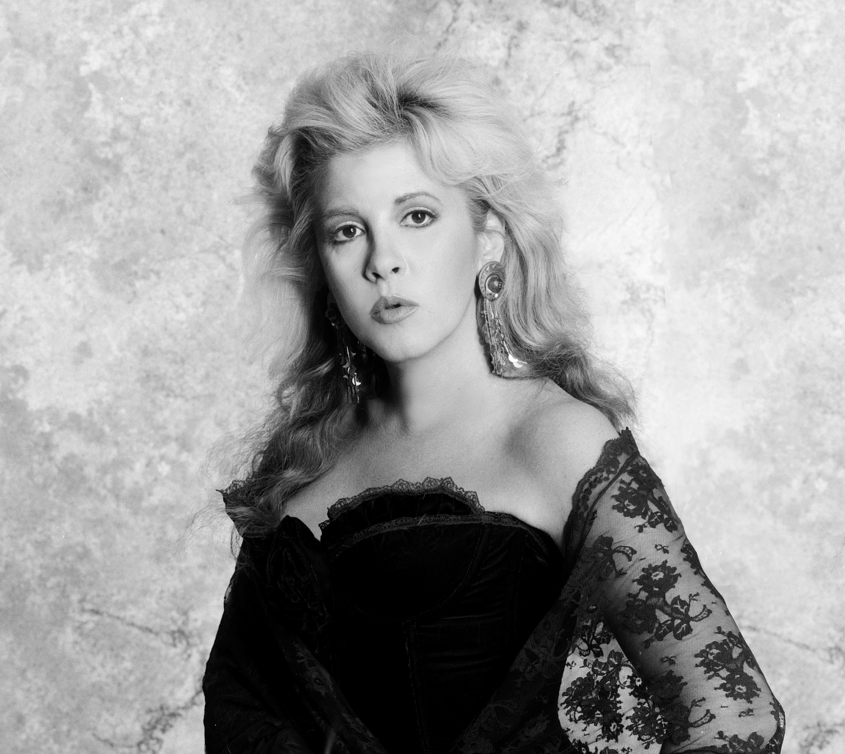 Stevie Nicks wears a black dress with lace sleeves and long earrings. 
