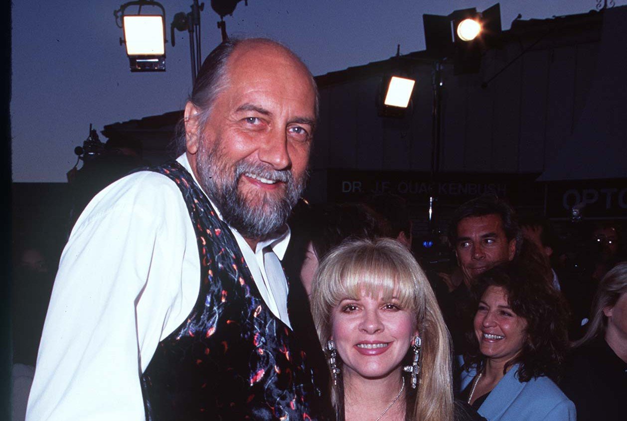 Mick Fleetwood wears a white shirt and a black vest. Stevie Nicks wears a black dress.