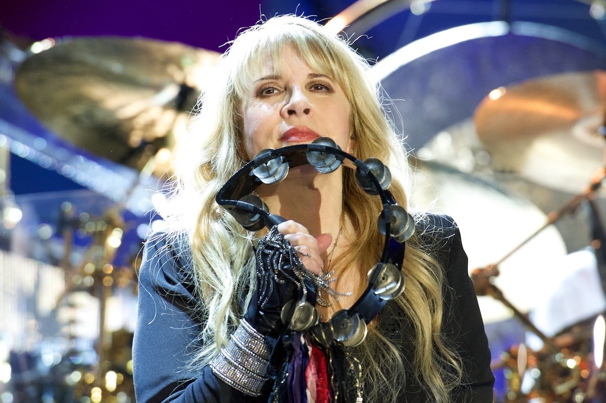 Stevie Nicks holds a tambourine up to her face.