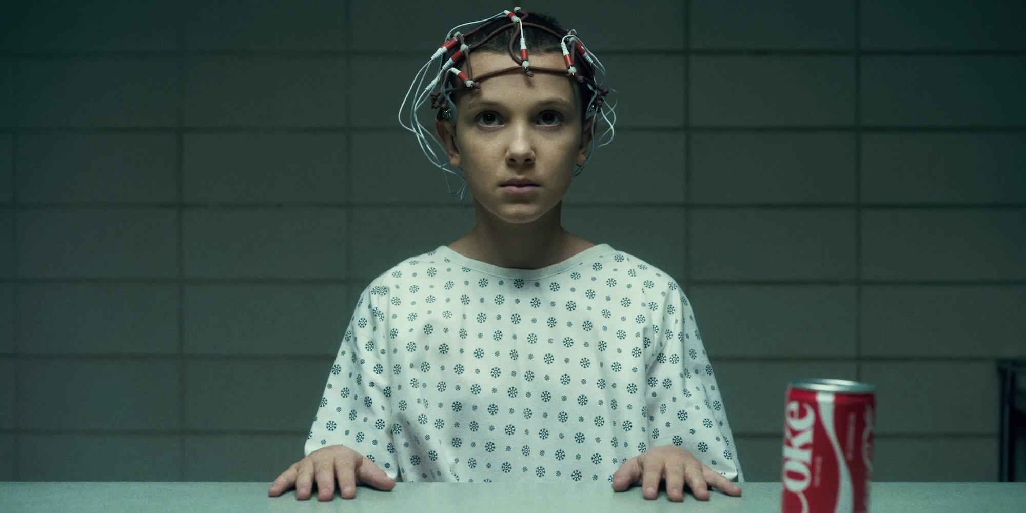'Stranger Things' star Millie Bobby Brown as Eleven in a production still from season 1 with wires attached to her head while wearing a hospital gown