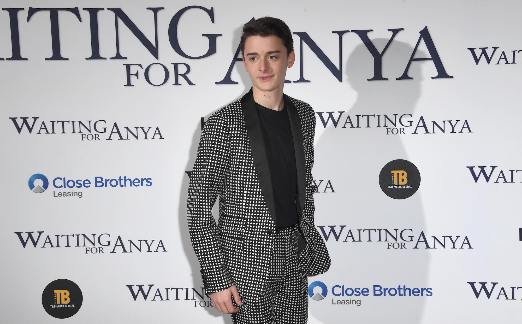 'Stranger Things' star Noah Schnapp in a gray suit with a black shirt underneath posing at an event.