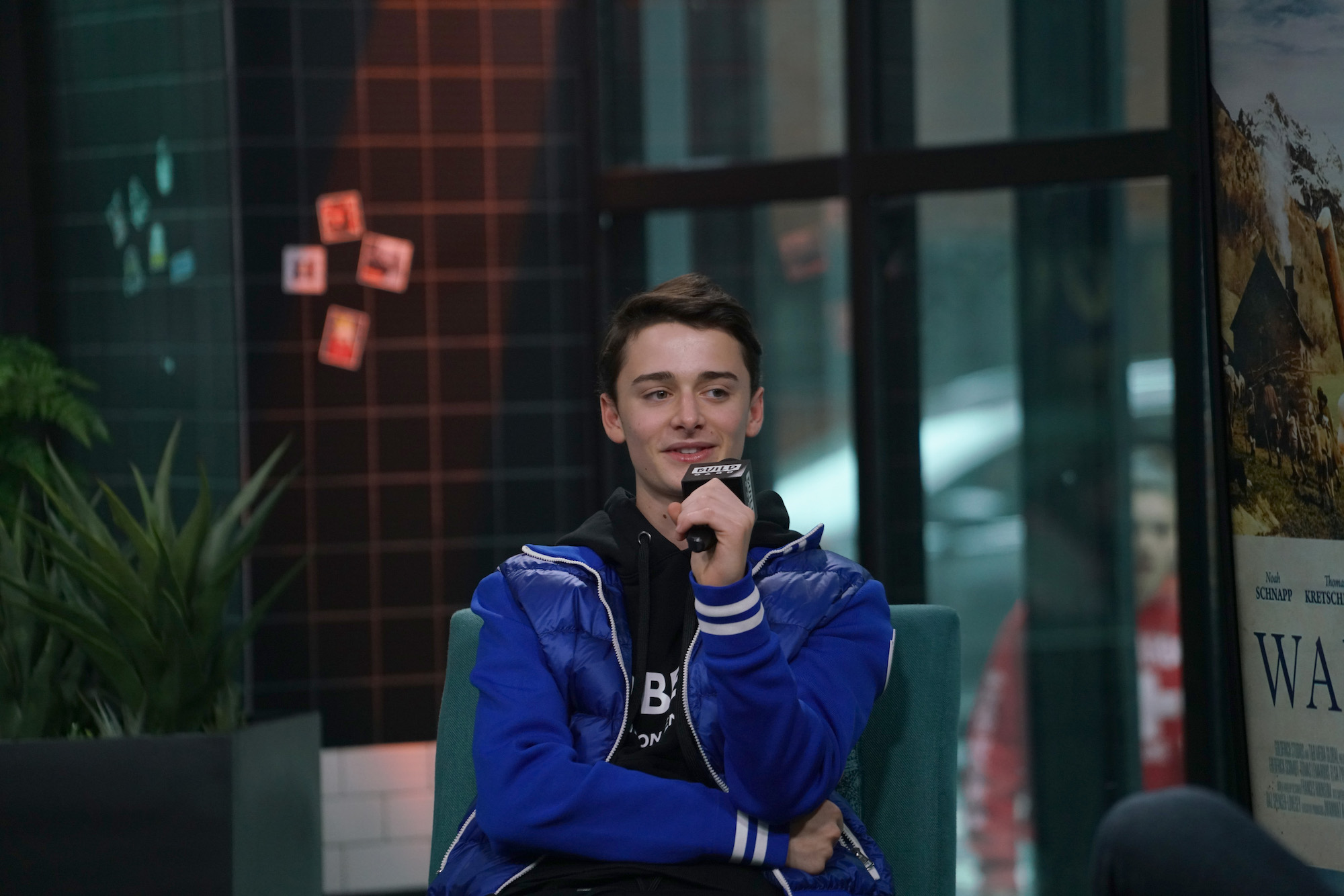Noah Schnapp, star of 'Stranger Things' Season 4, in a blue jacket and black pants holding a microphone.