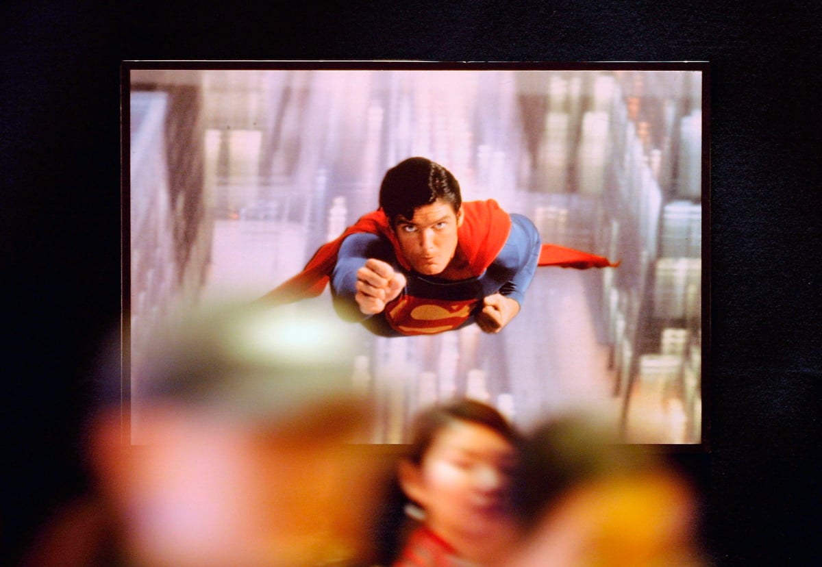 People walk under a poster of Superman, catchphrase 'Up, up and away,' during a ceremony to launch a joint venture to sell cut-rate DVDs
