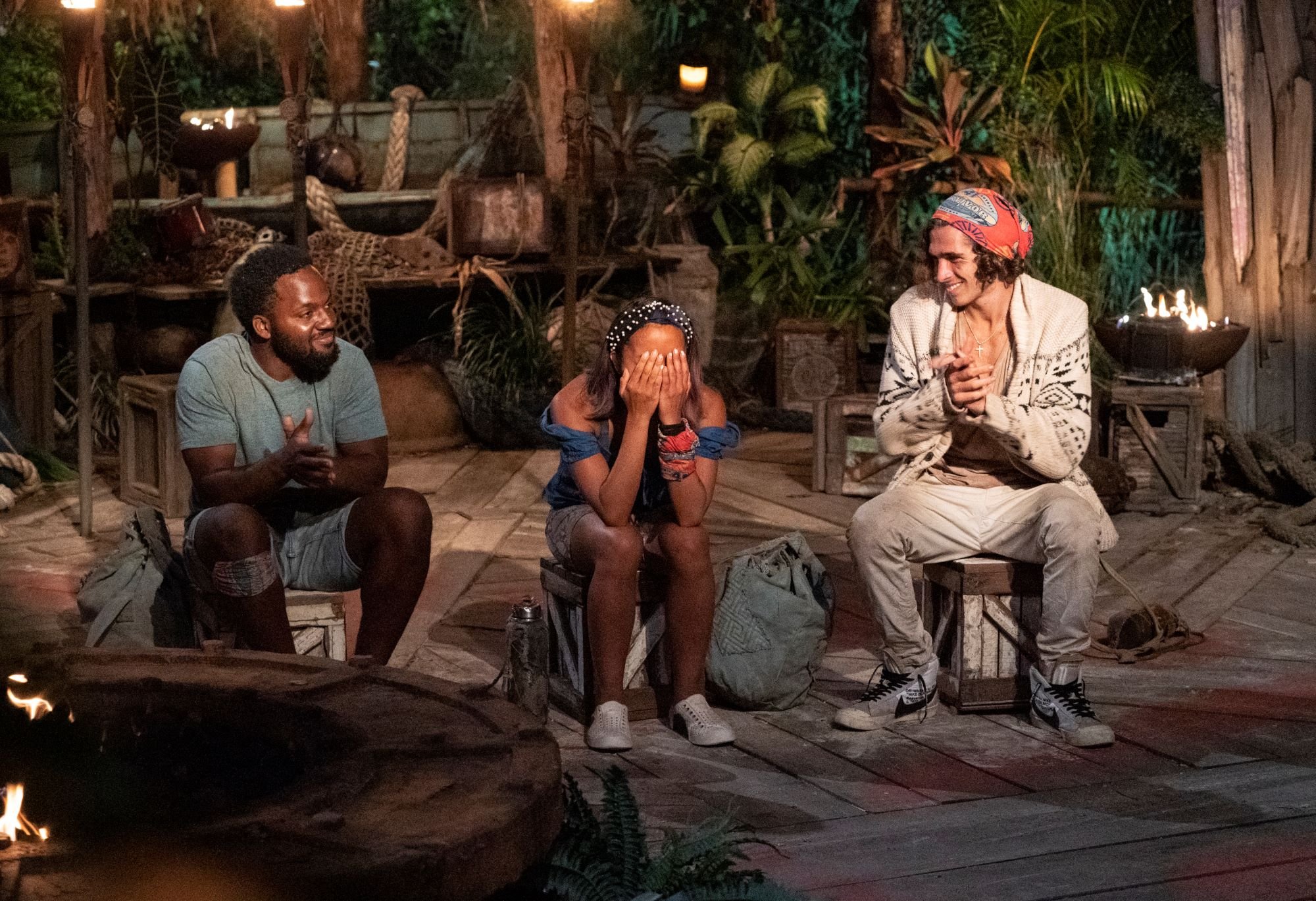 'Survivor' Season 41 stars Deshawn Radden, Erika Casupanan, and Xander Hastings are informed that Erika won. Deshawn wears a blue shirt and blue shorts. Erika wears a blue shirt and pearl-studded headband. Xander wears a white patterned cardigan and white pants. The 'Survivor' Season 42 preview shows the same format as season 41.