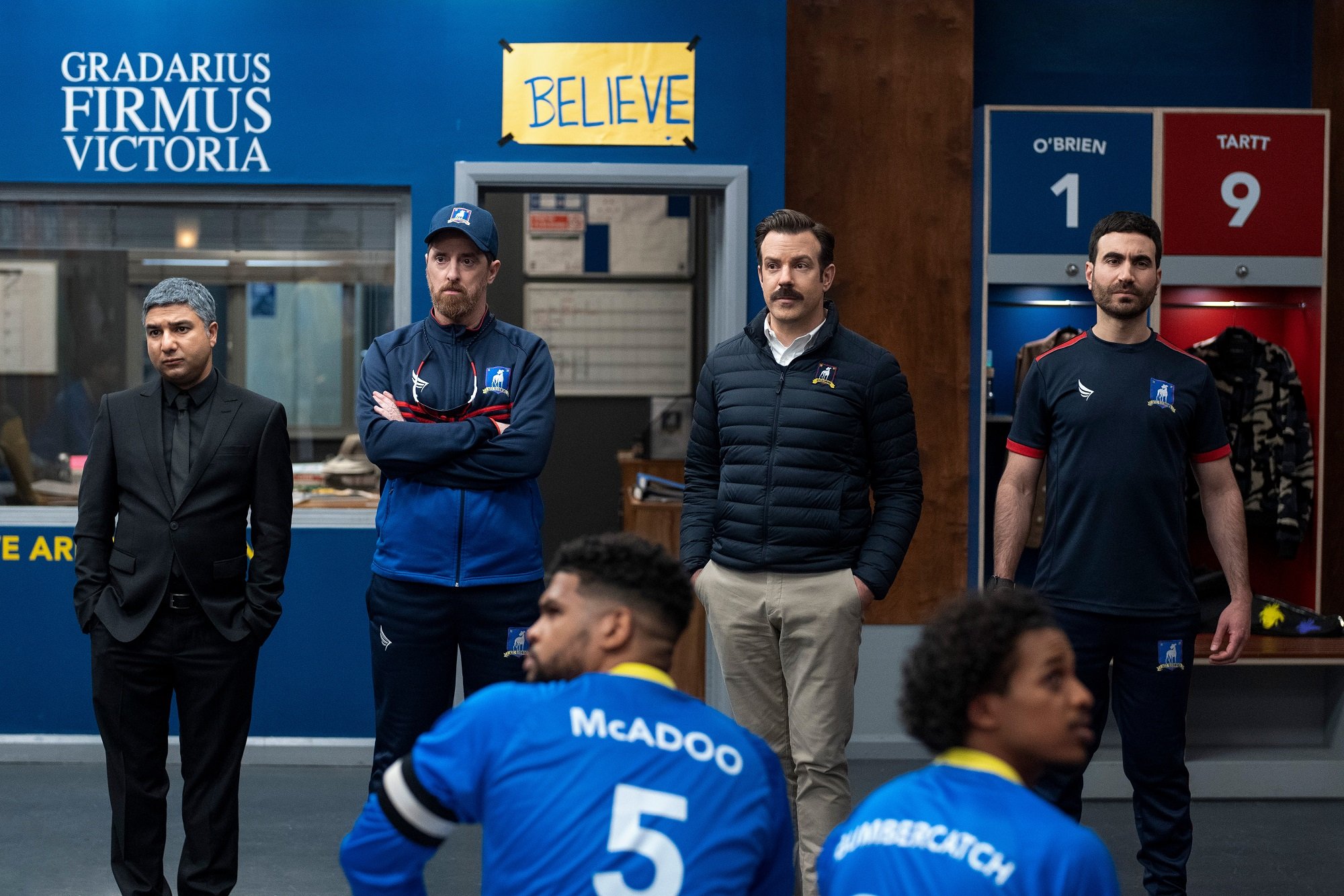 Nate, Coach Beard, Ted Lasso, and Roy Kent stand in the AFC Richmond locker room in 'Ted Lasso.' Season 3 is coming in 2022.