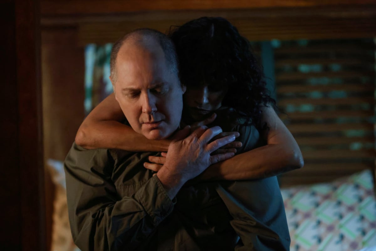 James Spader as Raymond Reddington and Karina Arroyave as Mierce Xiu in The Blacklist Season 9. Red sits in bed and Mierce puts her arms around him.