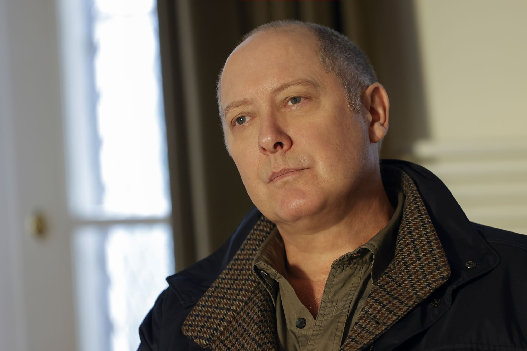 'The Blacklist' Season 9, which airs a new episode tonight, Dec. 9, stars James Spader as Raymond 'Red' Reddington. In the photo, Spader, in character as Red, wears a black coat over a brown and black jacket and a green button-up shirt.