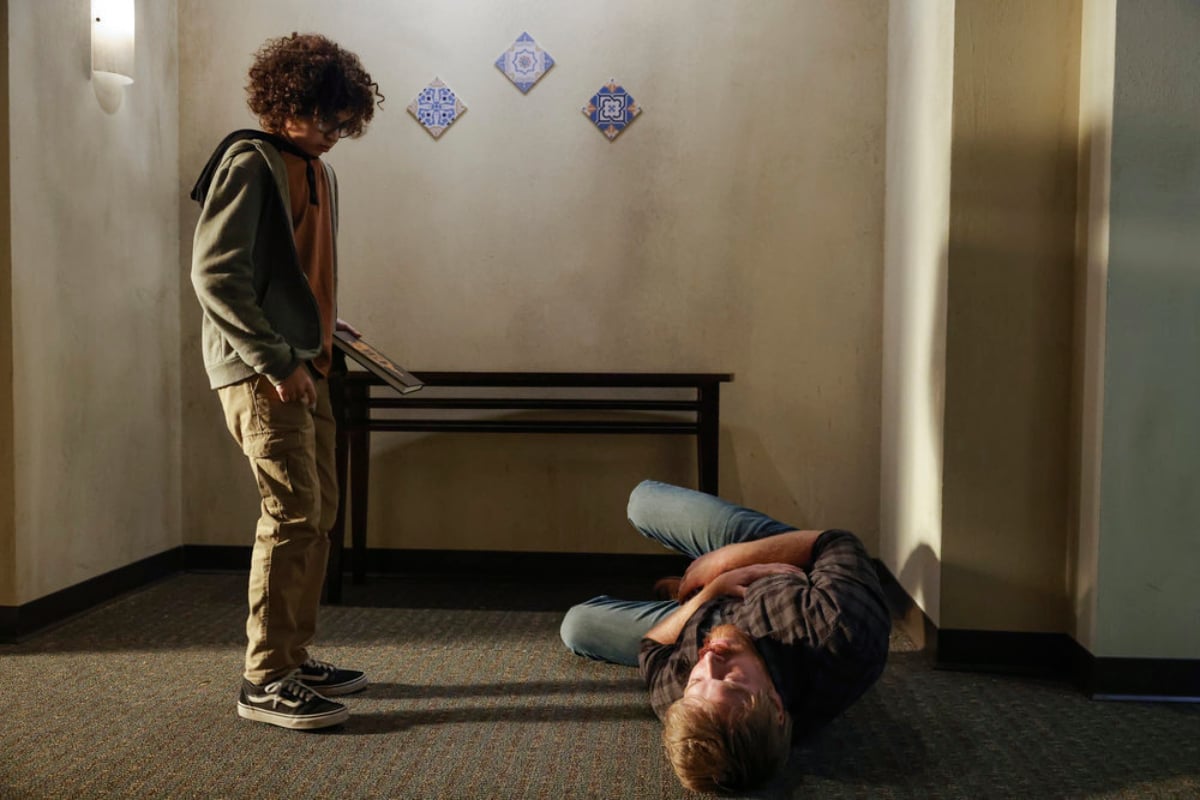 Dean Scott Vasquez as Theodore and Diego Klattenhoff as Donald Ressler in The Blacklist Season 9. Ressler lays on the ground in front of the kid.