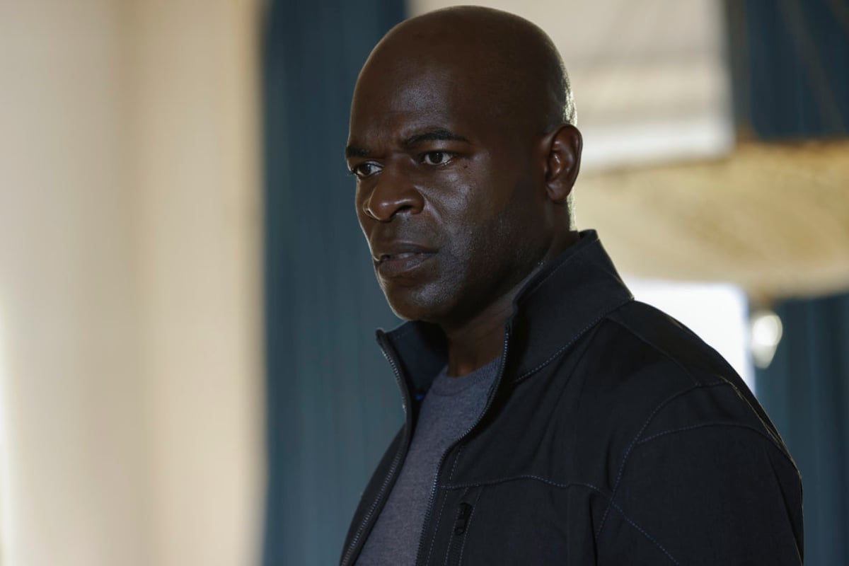 Hisham Tawfiq as Dembe Zuma in 'The Blacklist' Season 9. Dembe is wearing a blue t-shirt and black jacket.