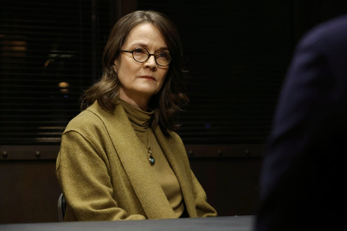 Enid Graham as Dr. Roberta Sand in The Blacklist Season 9 Episode 6. Sands is wearing a mustard-colored turtle neck sweater and round glasses.