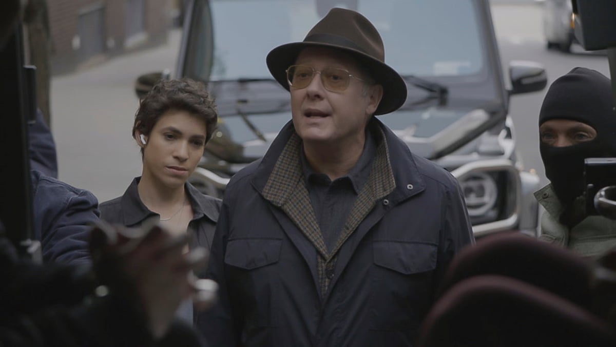 Diany Rodriguez as Weecha Xiu and James Spader as Red in The Blacklist Season 9. Red is talking to someone with Weecha and armed guards behind him.