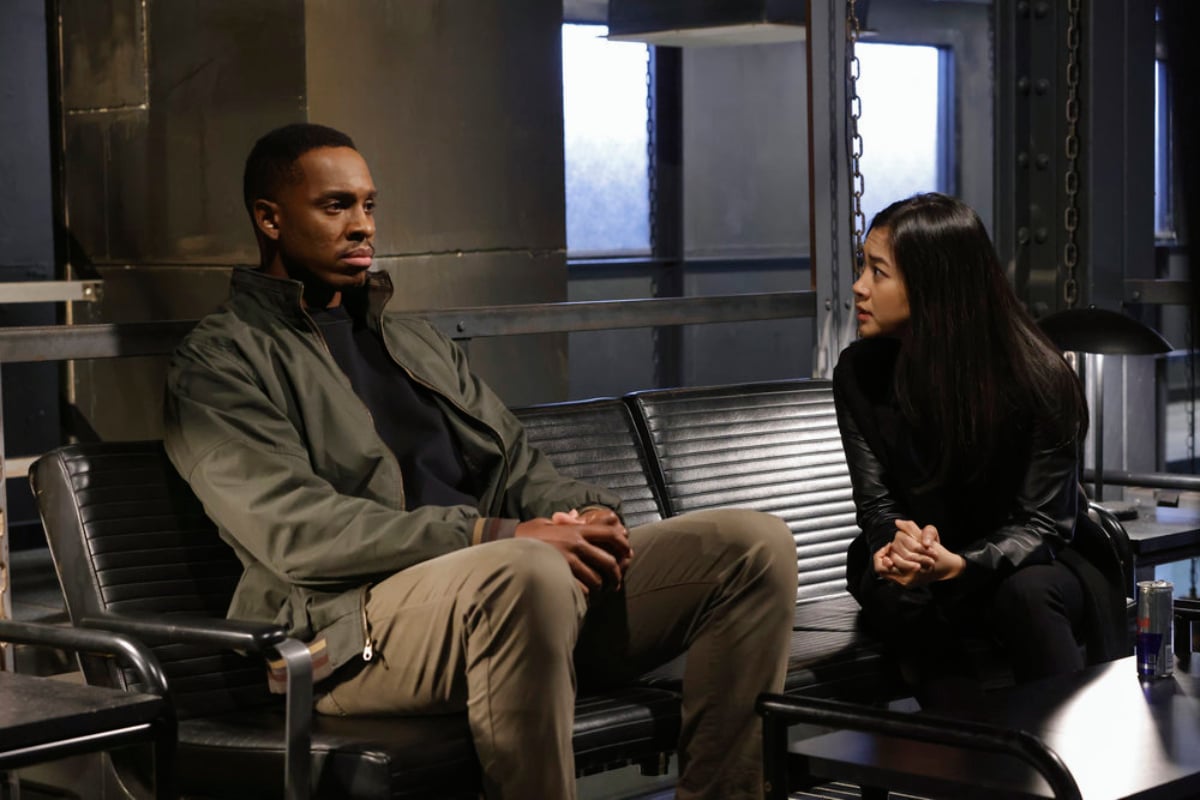 Colby Lewis as Peter Simpson and Laura Sohn as Alina Park in The Blacklist Season 9. Peter and Park sit next to each other on a bench.