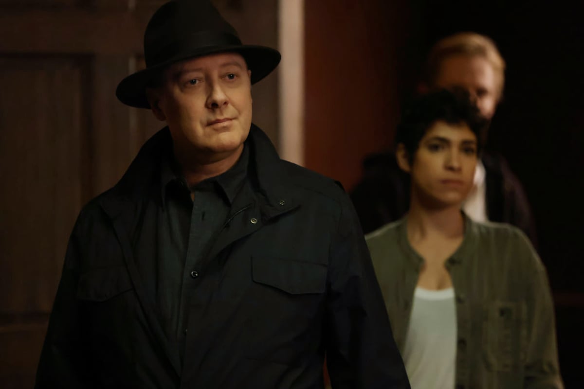 James Spader as Red and Diany Rodriguez as Weecha in The Blacklist Season 9. Red is wearing a hat and Weecha is standing behind him.