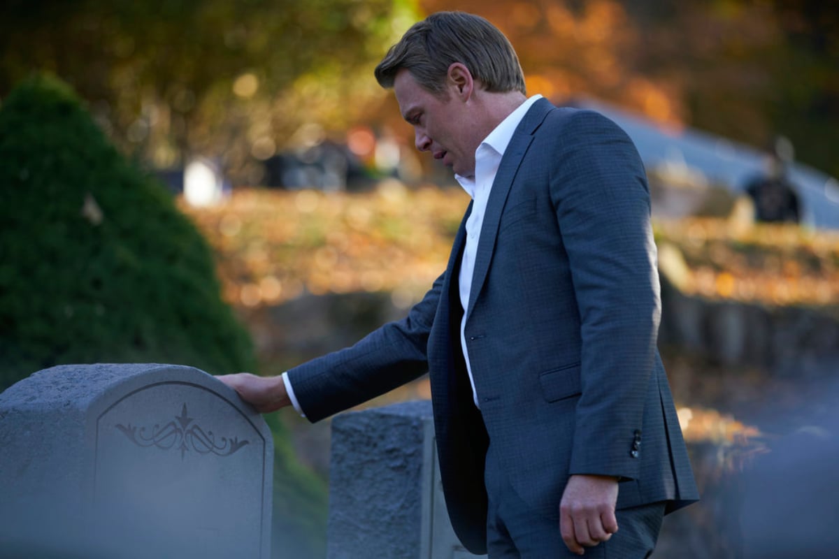Diego Klattenhoff as Donald Ressler in The Blacklist Season 9. A clean-shaven Ressler in a suit puts his hand on a tombstone.