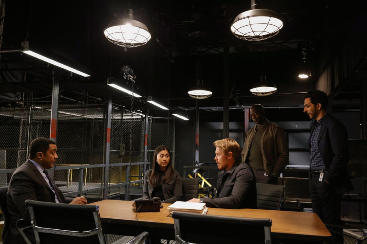 Harry Lennix as Harold Cooper, Laura Sohn as Alina Park, Diego Klattenhoff as Donald Ressler, Hisham Tawfiq as Dembe Zuma, adn Amir Arison as Aram Mojtabai in The Blacklist Season 9. The task force stand/sit around a table.