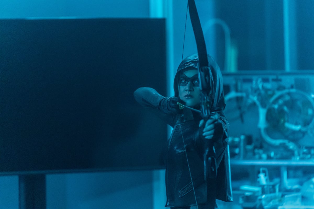 'The Flash' Season 8 Episode 5 star Katherine McNamara, in character as Mia Queen, wears her Green Arrow costume and notches an arrow in her bow and aims it.