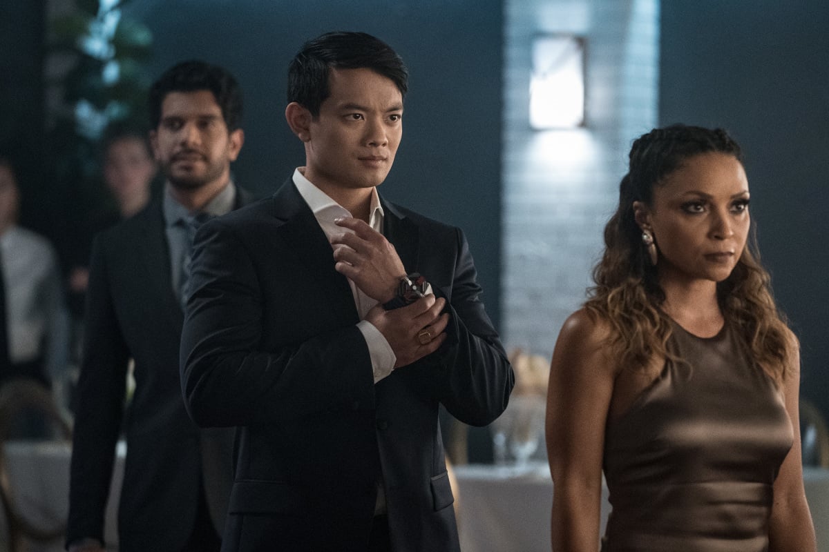 'The Flash' Season 8 Episode 4 actors Osric Chau and Danielle Nicolet, as their comic book characters Ryan Choi and Cecile Horton, stand side-by-side. Ryan wears a black suit over a white button-up shirt and a high-tech watch. Cecile wears a brown dress.