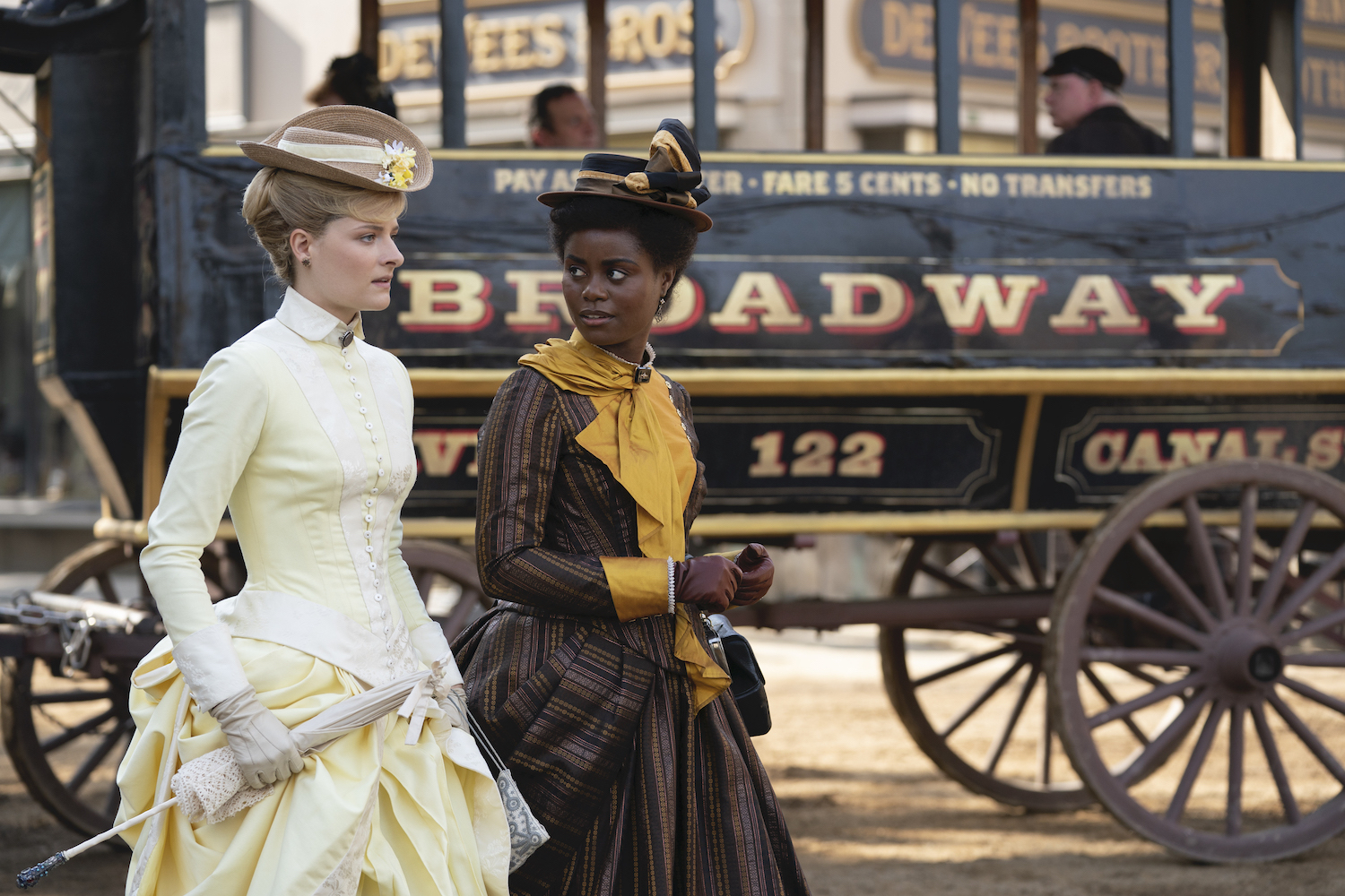 Louisa Jacobsen and Denee Benton, both wearing late 19th century dresses, in front of an omnibus
