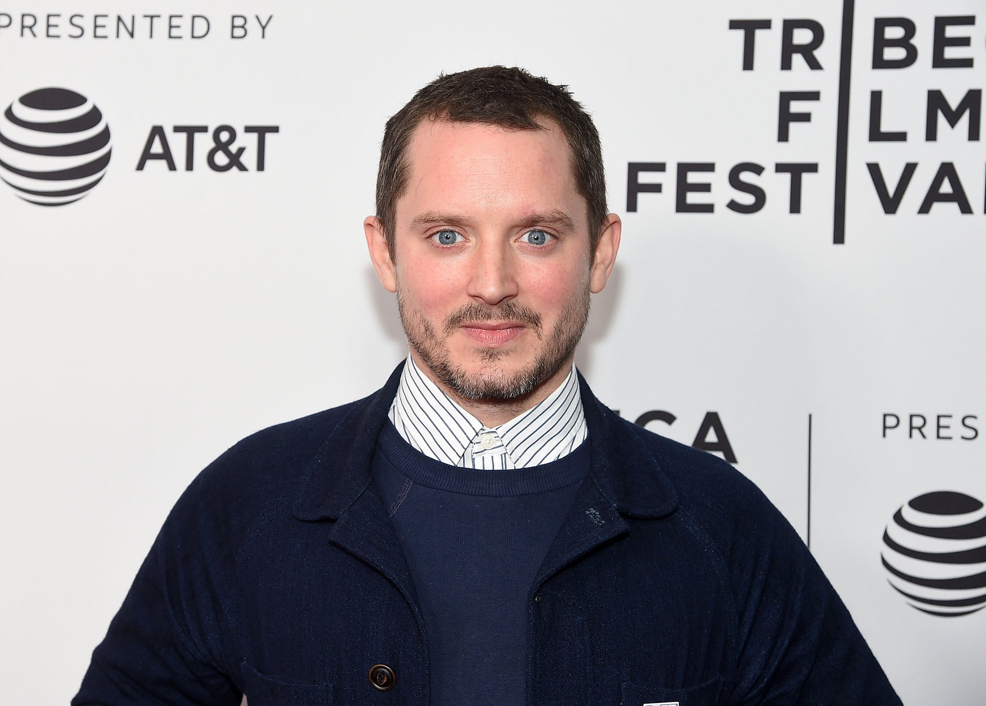 'The Lord of the Rings' star Elijah Wood in a jacket in front of a step and repeat