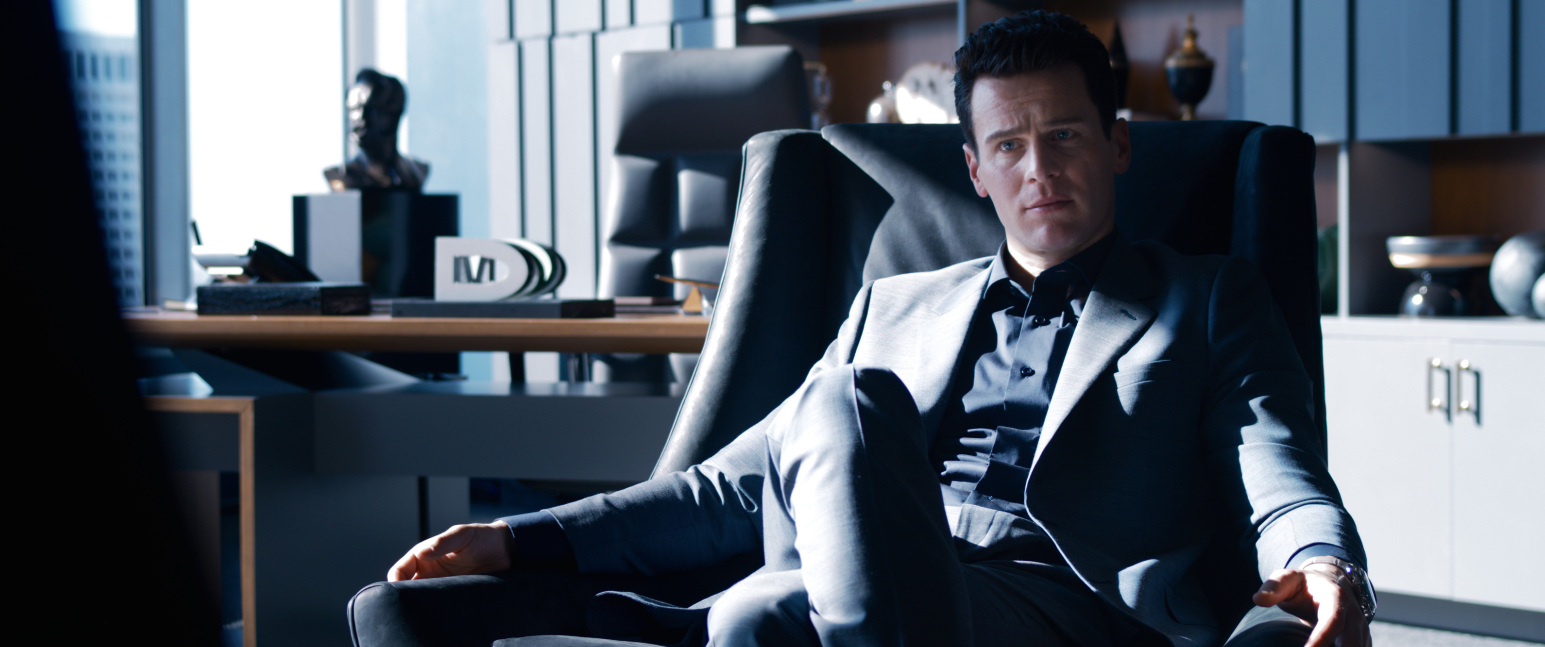 'The Matrix Resurrections' actor Jonathan Groff as Agent Smith wearing a suit sitting in a leather chair