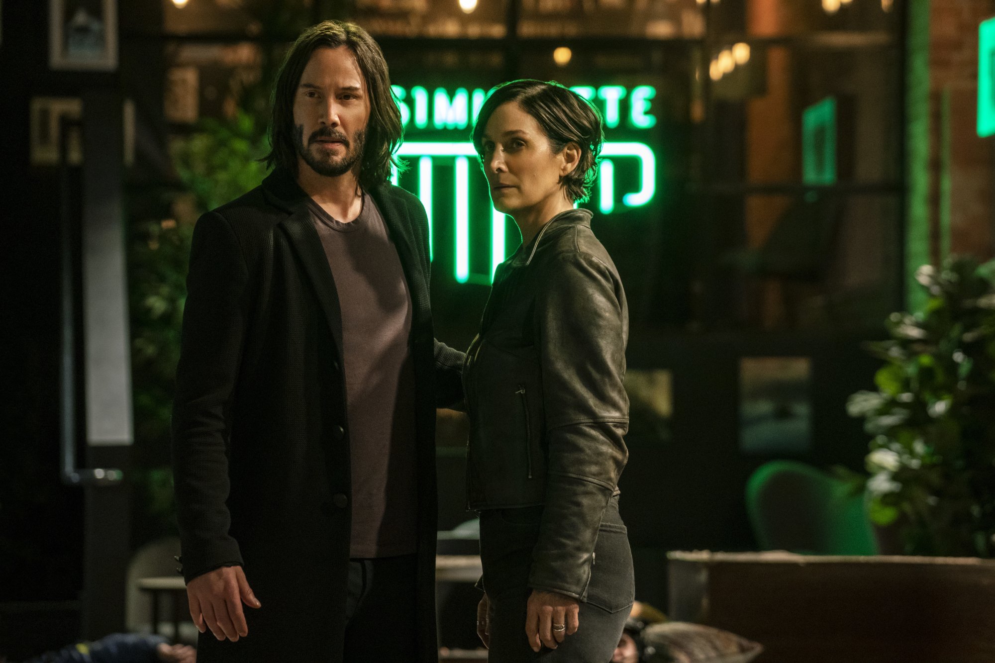 'The Matrix Resurrections' review Keanu Reeves as Neo/Thomas A. Anderson and Carrie-Anne Moss as Trinity/Tiffany standing in front of neon sign