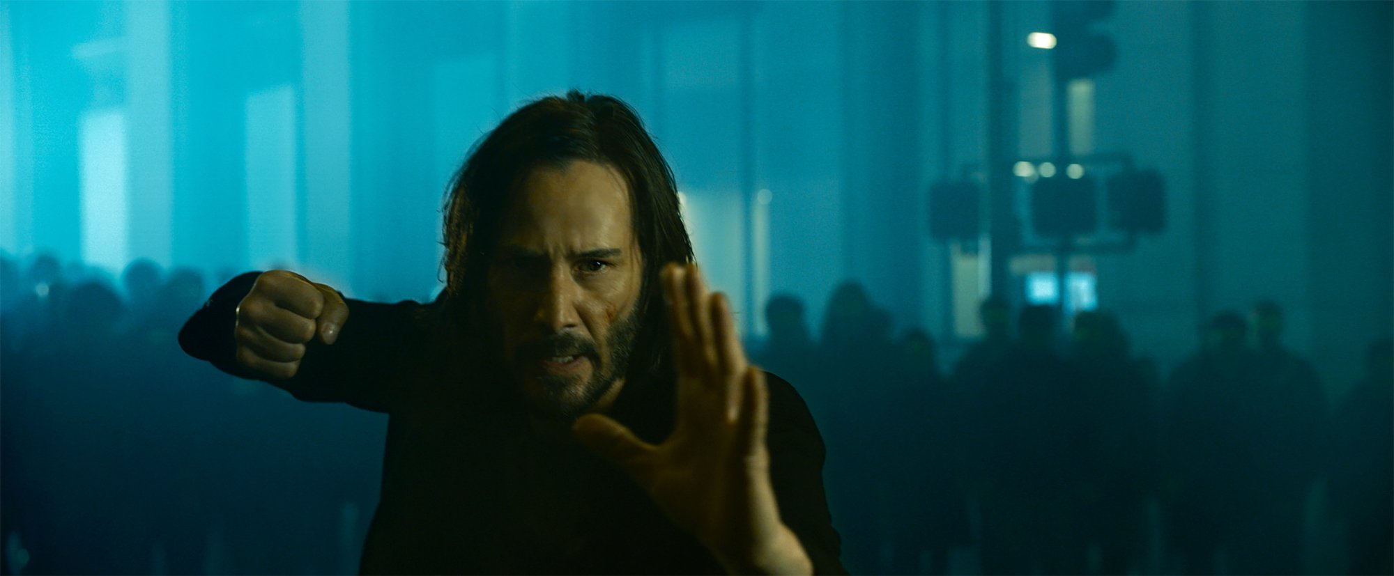 'The Matrix Resurrections' review Keanu Reeves as Neo:Thomas A. Anderson with a fist raised and his hand out in front with a mob of people behind him