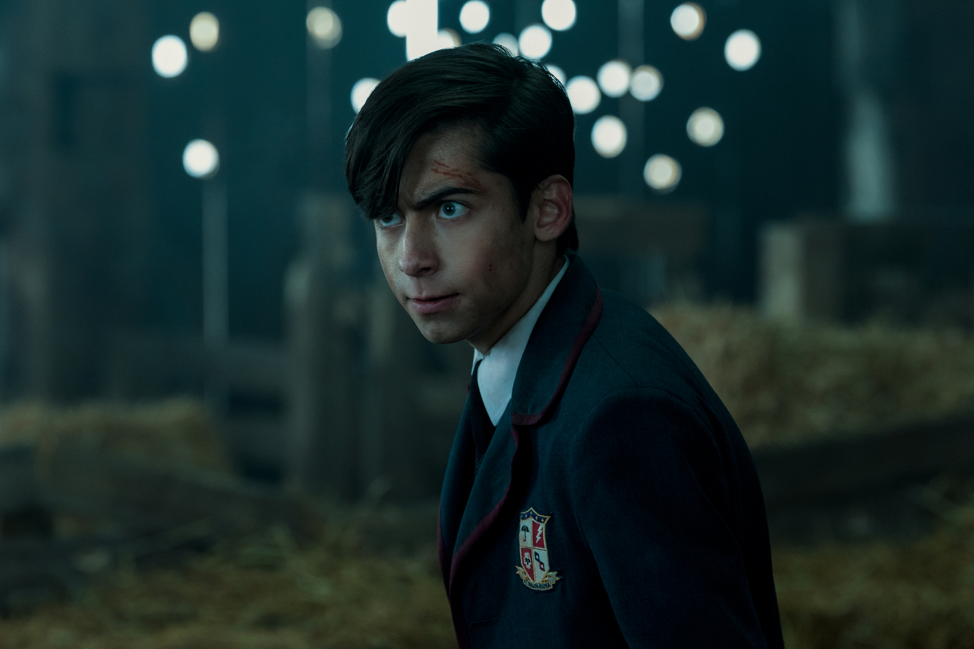 'The Umbrella Academy' character Number Five, played by Aiden Gallagher, standing in a bard in his uniform with scratches on his face.