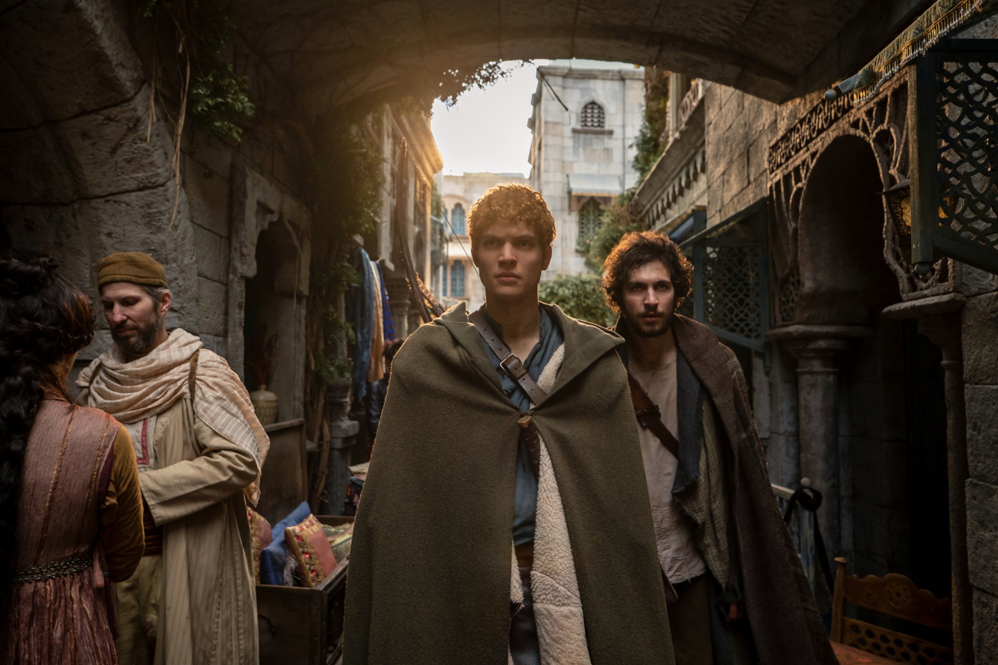 Josha Stradowski as Rand al’Thor and Barney Harris as Mat Cauthon in 'The Wheel of Time' Episode 5. They're walking through a crowded town.