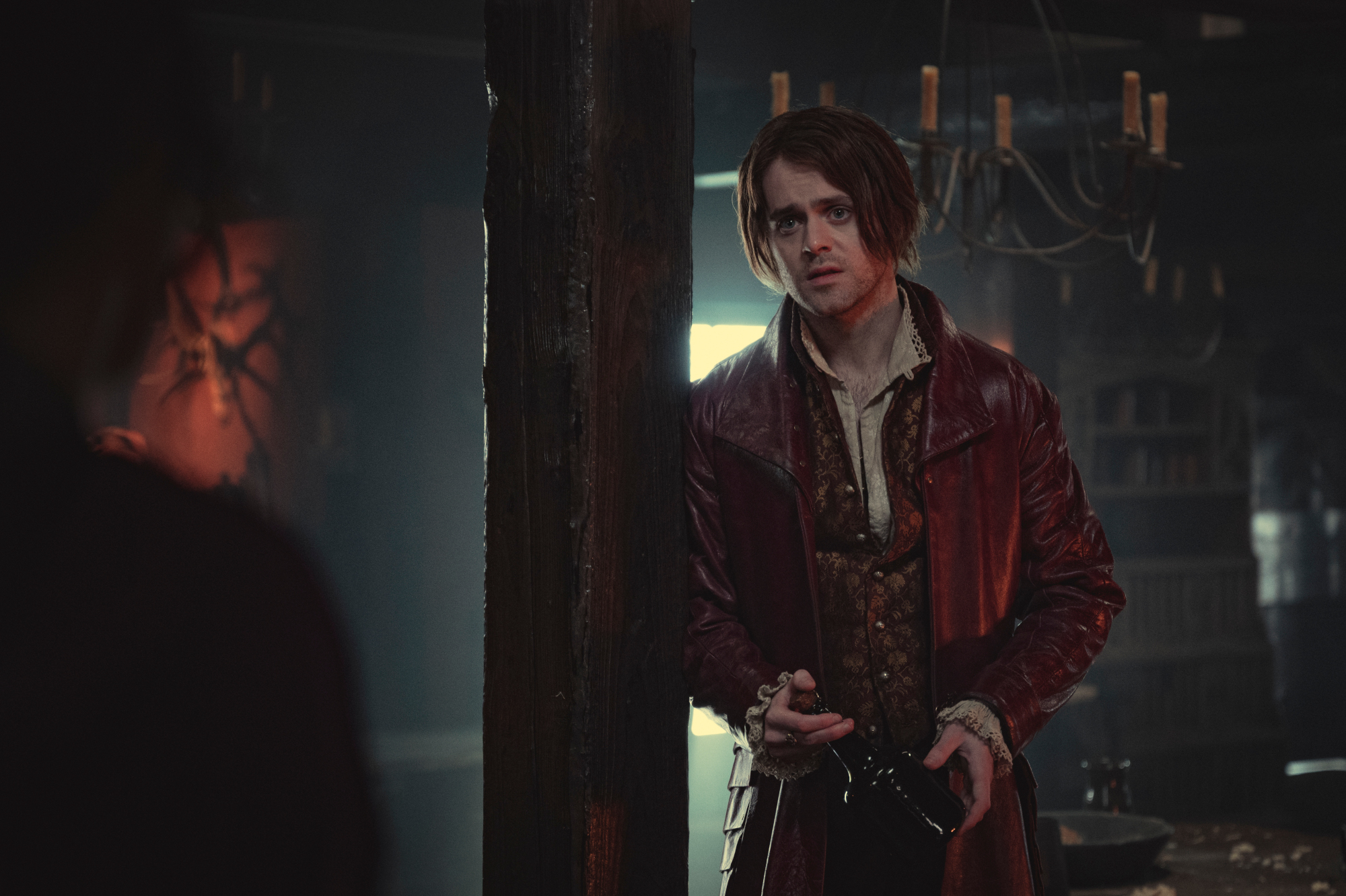 Joey Batey as Jaskier in 'The Witcher' Season 2 on Netflix. He's wearing a red leather coat and his hair is longer than in season 1.