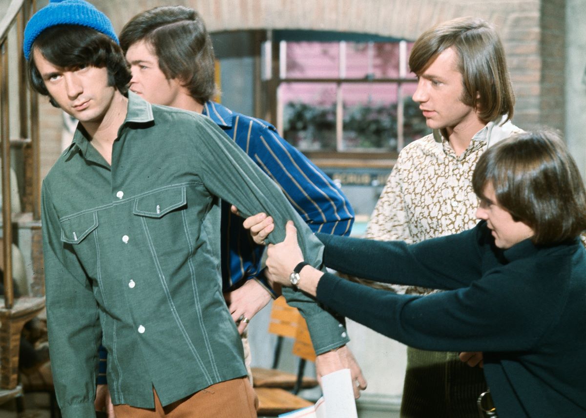 The Monkees, Mike Nesmith in a blue wool cap, leaning away as Davy Jones pulls on his arm. Peter Tork and Micky Dolenz stand in the background.