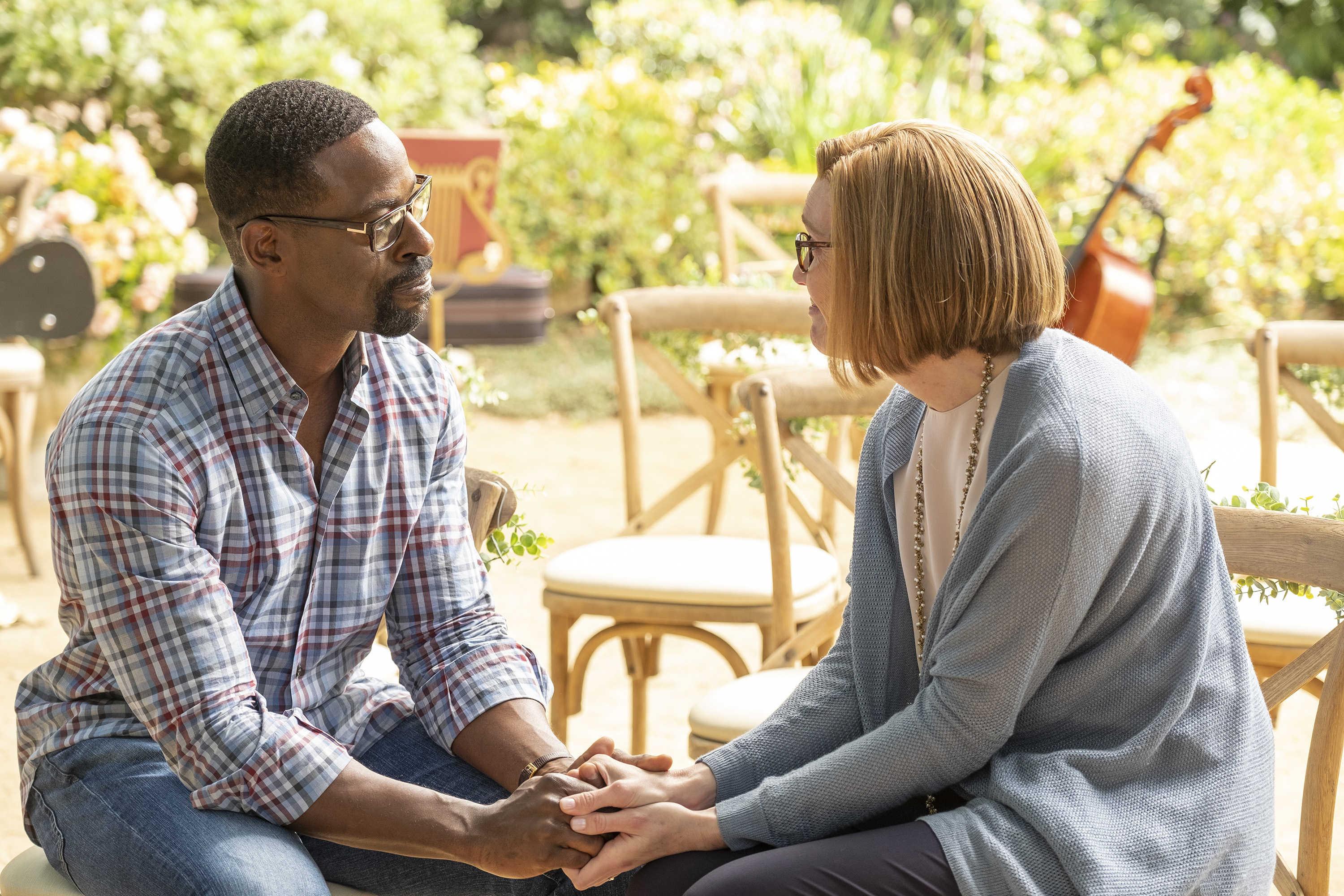 'This Is Us' Season 6 stars Sterling K. Brown and Mandy Moore, in character as Randall and Rebecca, hold hands as they talk. Randall wears a blue and red plaid shirt and jeans. Rebecca wears a blue cardigan over a white shirt and black pants.