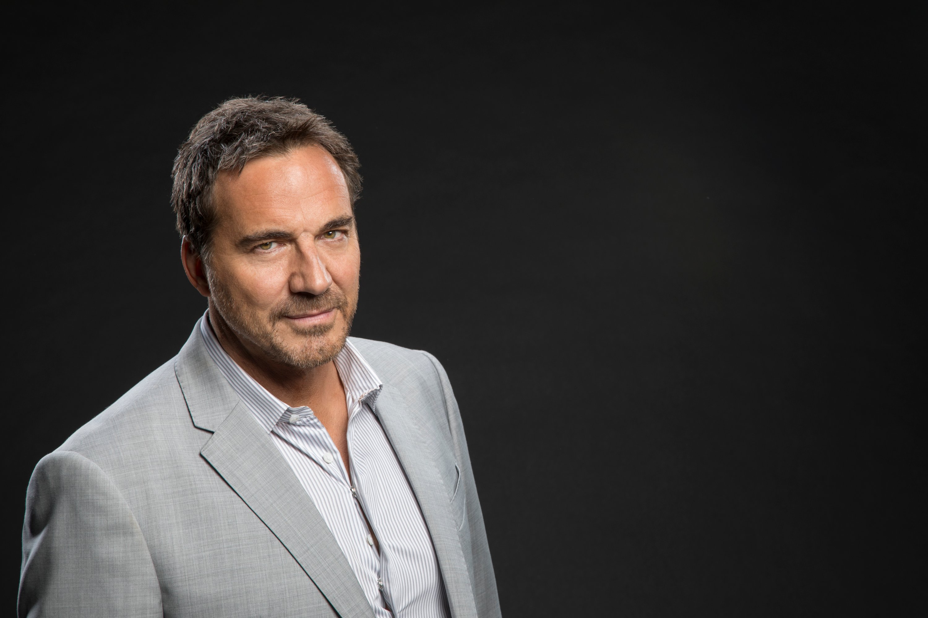 'The Bold and the Beautiful' actor Thorsten Kaye wearing a grey suit and white shirt; and standing in front of a black backdrop.