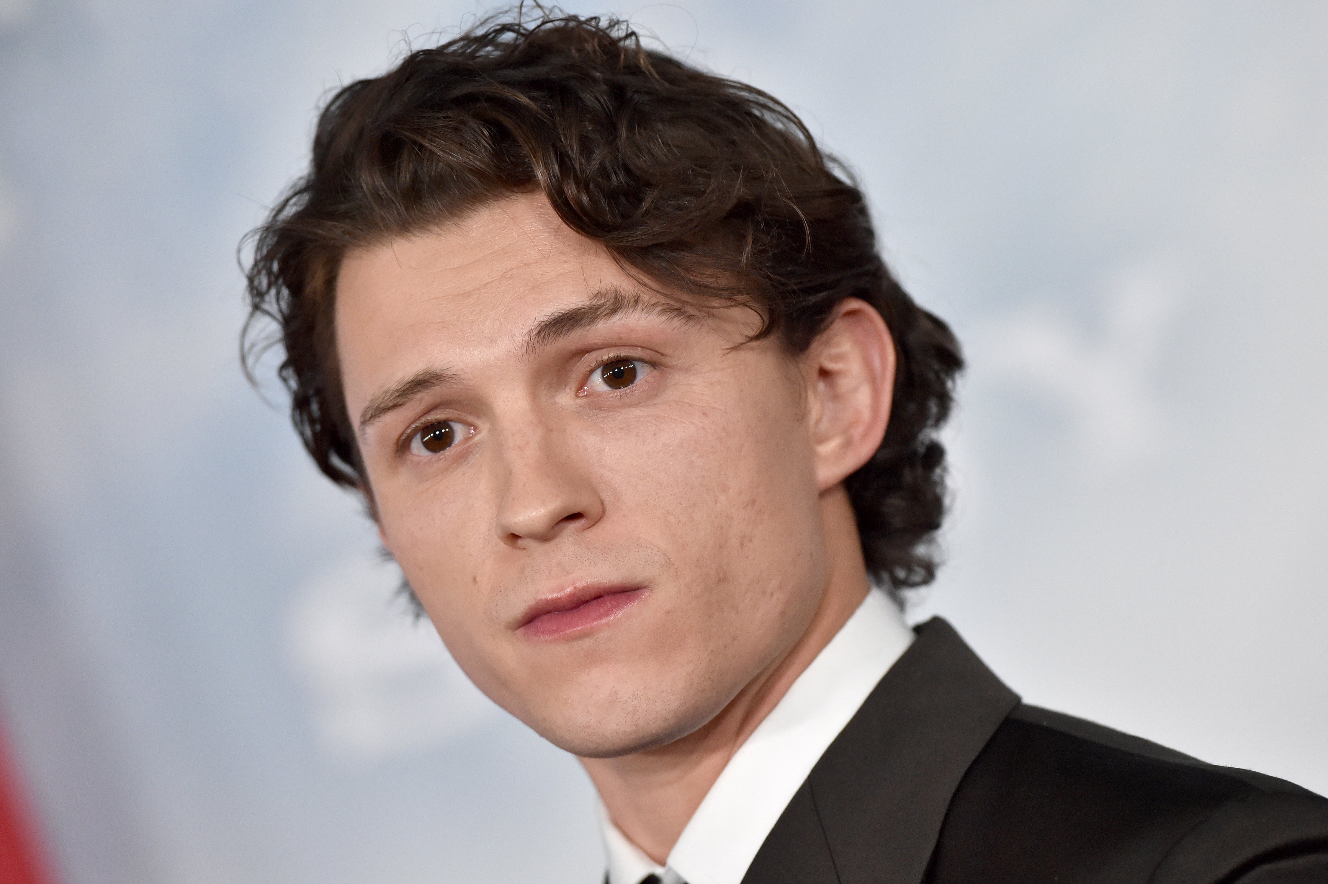 'Spider-Man: No Way Home' star Tom Holland, who wants his character to fight Morbius, wears a dark gray suit over a white button-up shirt and black tie.