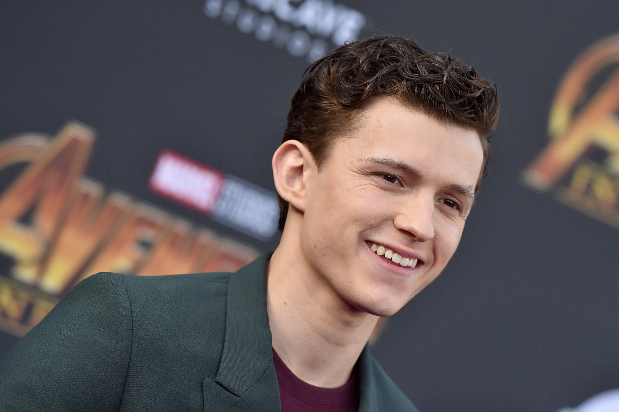 Tom Holland on the red carpet for the 'Avengers: Infinity War' premiere. He's wearing a black jacket and staring to the side of the camera.